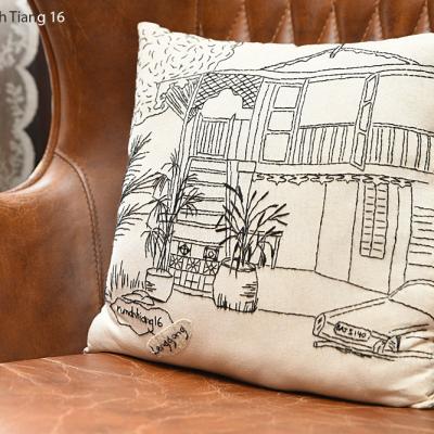 A hand-stitched illustration of Rumah Tiang 16 on a cushion cover.